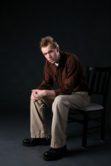 young man sitting thoughtfully on chair with his arms resting