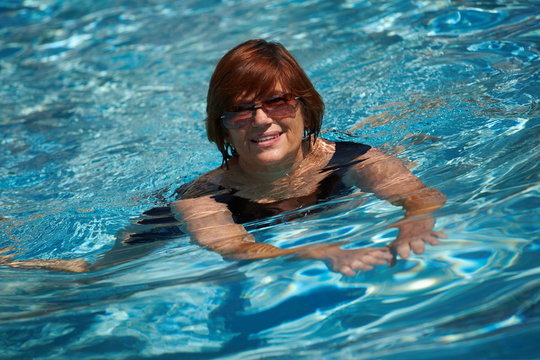 Happy active senior woman ( 60s ) swimming in pool
