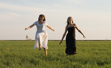 Two beautiful girls running on the green field