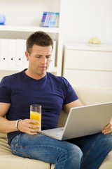 Man sitting on sofa at home and using laptop computer.