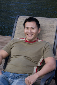 Asain man sitting in a lounge chair on a dock.