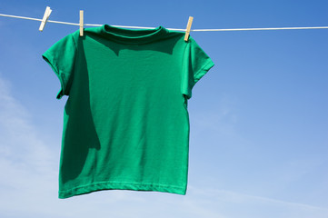A green t-shirt hanging on a clothesline in front of a blue sky