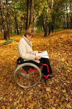 Woman on wheelchair reading a magazine in the park