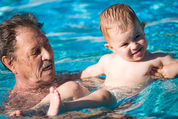 Grandfather and grandson swimming together in the pool.