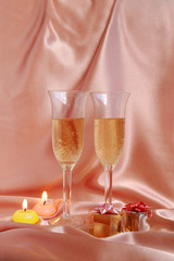 Pair of champagne flutes with candles and gift box on silk