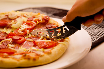 pepperoni Pizza being cut with a pizza knife. © willmetts