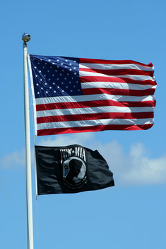 A American and POW flags against a blue sky