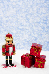 Nutcracker sitting on snow with three red presents