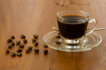 a cup of dark coffee with beans over wood background