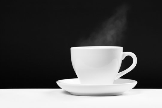 white cup with hot beverage over black background