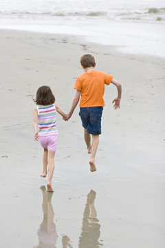 two children running hand in hand on beach