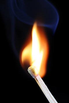 Burning fire of match on black background with blue smoke