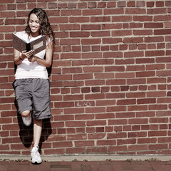 Beautiful young girl reading notebook against a brick wall.