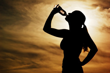 Beautiful young sporty woman drinking in front of a sunset.