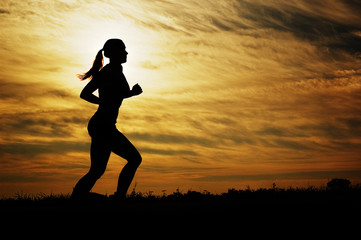 Beautiful young woman running in front of a sunset.