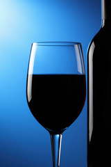 A glass of red wine and bottle, blue graduated background.
