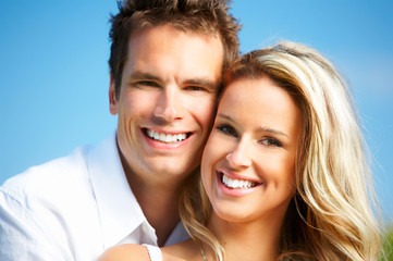 Young love couple smiling under blue sky.