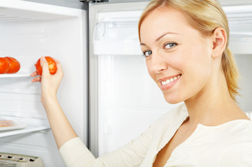 The smiling blonde takes a tomato from a refrigerator