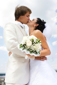 Bride and groom kissing on the blue sky background