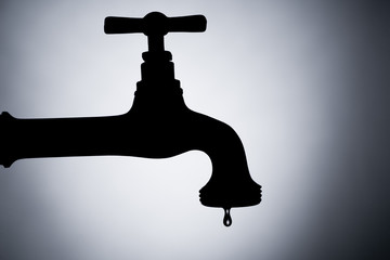 a silhouette of a leaking tap against bluish background
