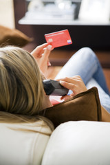 Young woman relaxing at home on the phone with credit card..