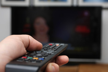 Human hand holding a remote control poined at flat screen tv