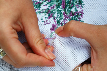 Fingers of young women, cross embroidery.