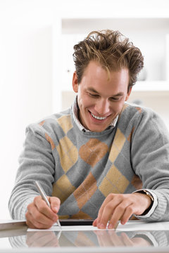 Happy young man writing on desk at home, smiling.