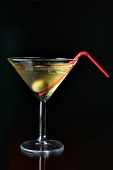 Cocktail glass with ice and olive close-up over black background