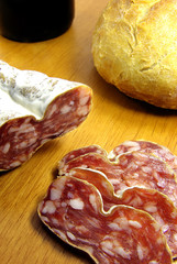 Sliced boloney, bread and wine on a wooden board.