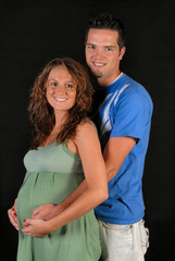 Portrait of happy and pregnant couple. His arms around her.