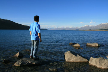 Fototapeta na wymiar A man on a rock overlooking a rich blue lake