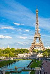 Eiffeltoren, met bewolkte blauwe lucht en zonnige bomen rond.