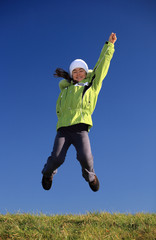 Young girl wearing winter jacket jumping against blue sky