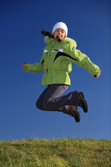 Young girl wearing winter jacket jumping against blue sky