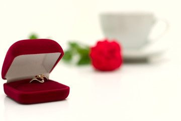 Box with a ring against a cup and a rose.