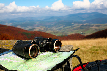 An image of binoculars and map on dry grass. Adventure theme