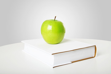 The green apple is on the book on a grey background