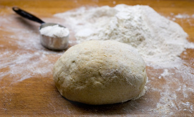 Kneaded dough and a measuring cup on wooden surface