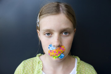 a sad girl with colorful bandages over her mouth