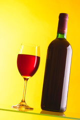 Glass and bottle of red wine on yellow background