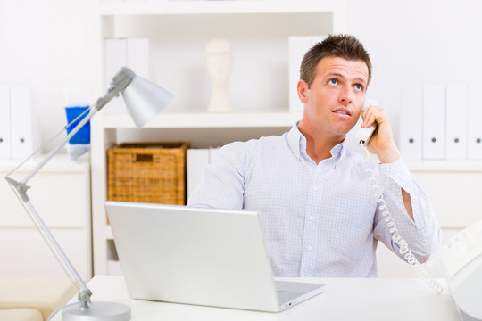 Business man working on computer at home calling on phone.