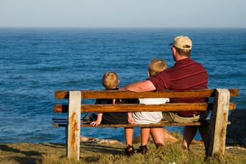 father and his two sons on a bench looking out over the ocean