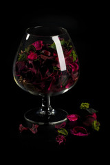 Dry rose petals and leaves are in the glass vase/