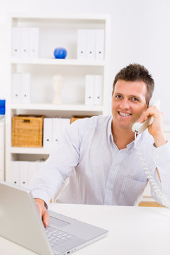 Business man working on computer at home calling on phone