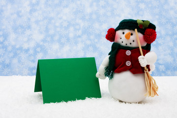 Snowman with a green blank card on snowflake background
