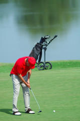 Golfer with red T-shirt putting on green golf course