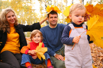 Family of four with yellow maple leaves in wood in autumn.