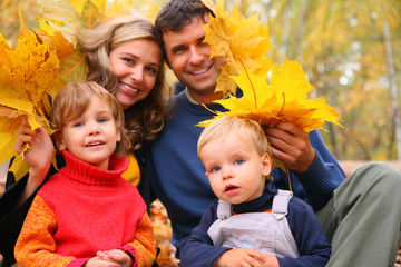 Family of four with yellow maple leaves in wood in autumn.