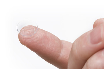 finger holding contact lens over white background